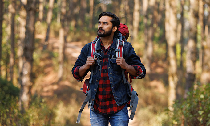 a man of Indian decent walking through the woods on a hiking trip
