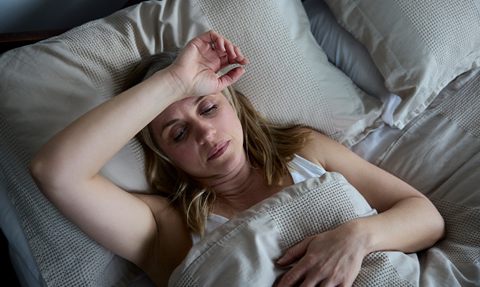 A woman laying in bed with her hand rested on her forehead