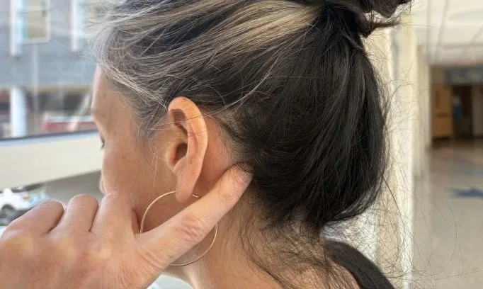 index finger on pressure point behind ear just above base of skull