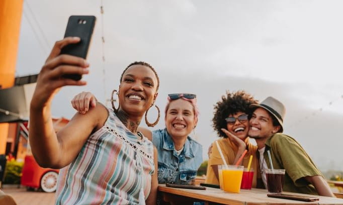 four friends sitting at picnic table taking selfie together