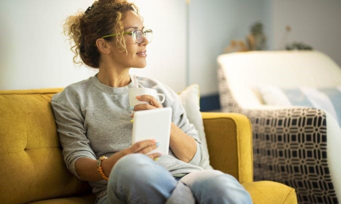 woman relaxing on couch with a digital book and hot drink